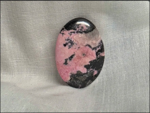 A Rhodonite cabachon that was cut and polished at TCM. It has a pink band through the center with black edges above and below.